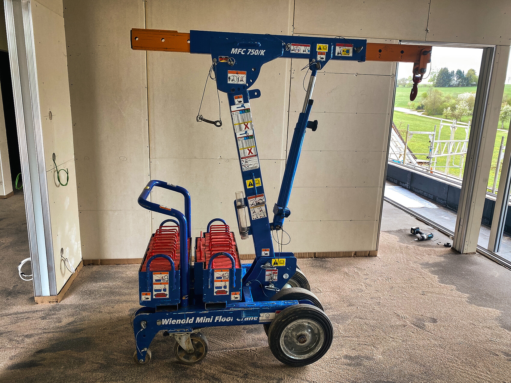 Small mobile construction crane on an interior finishing site with wall panels and open window opening