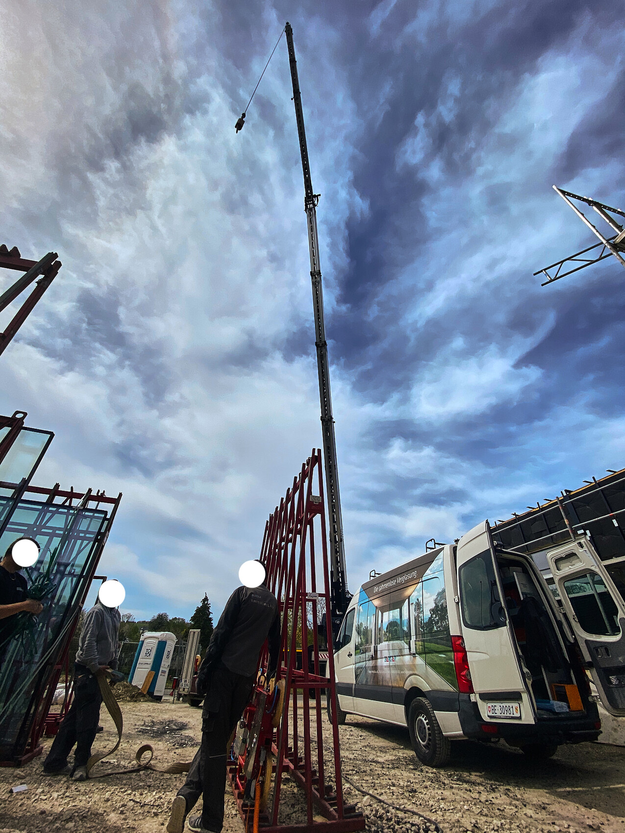 Construction site with tall crane, red steel scaffolding, workers and van in the background