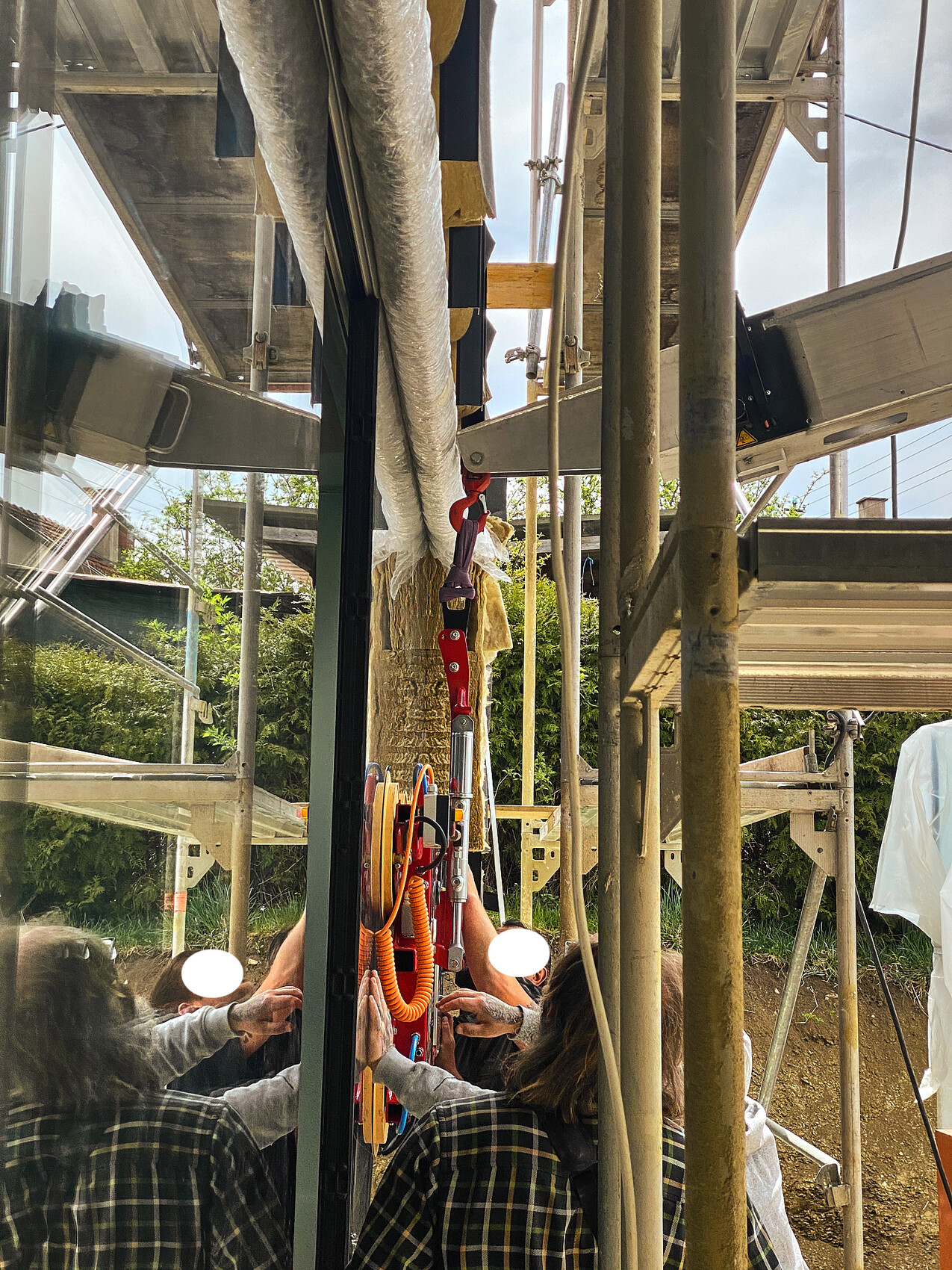 Several workers attaching a red safety device to the scaffolding in front of a glass facade.