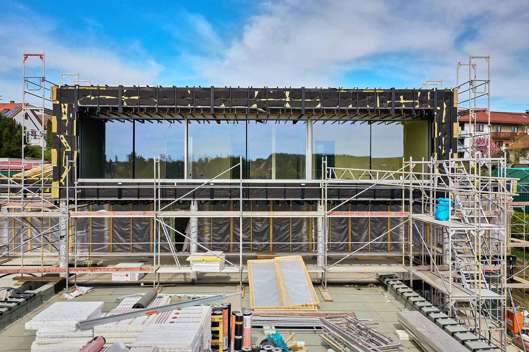 Construction site with scaffolding around modern building with large glass fronts and black insulation