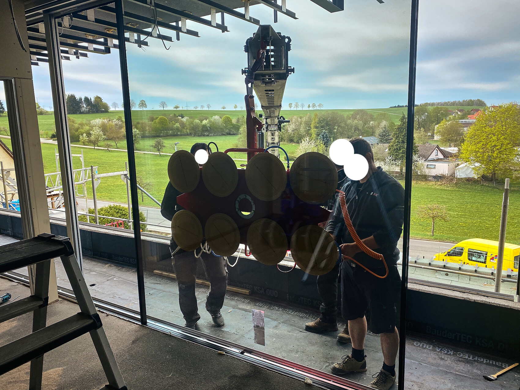 Two workers installing a glass panel with suction cups into a glass facade.