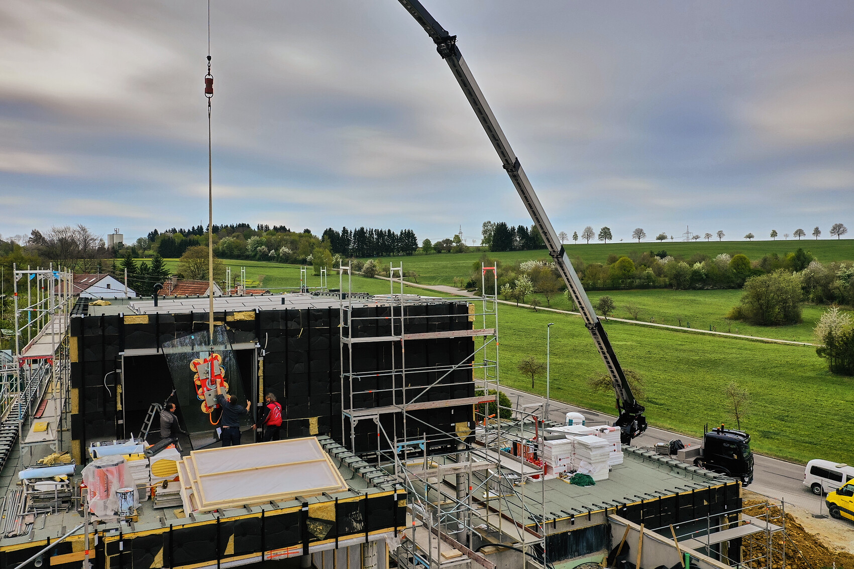 Construction site with crane, scaffolding and workers on shell construction on green land.