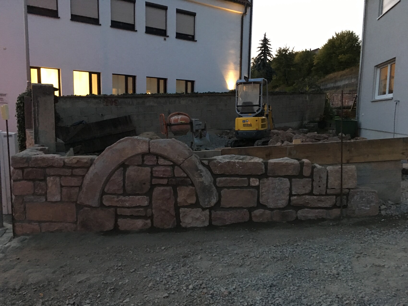 Construction site with natural stone wall in the foreground, mini excavator and concrete mixer in the background