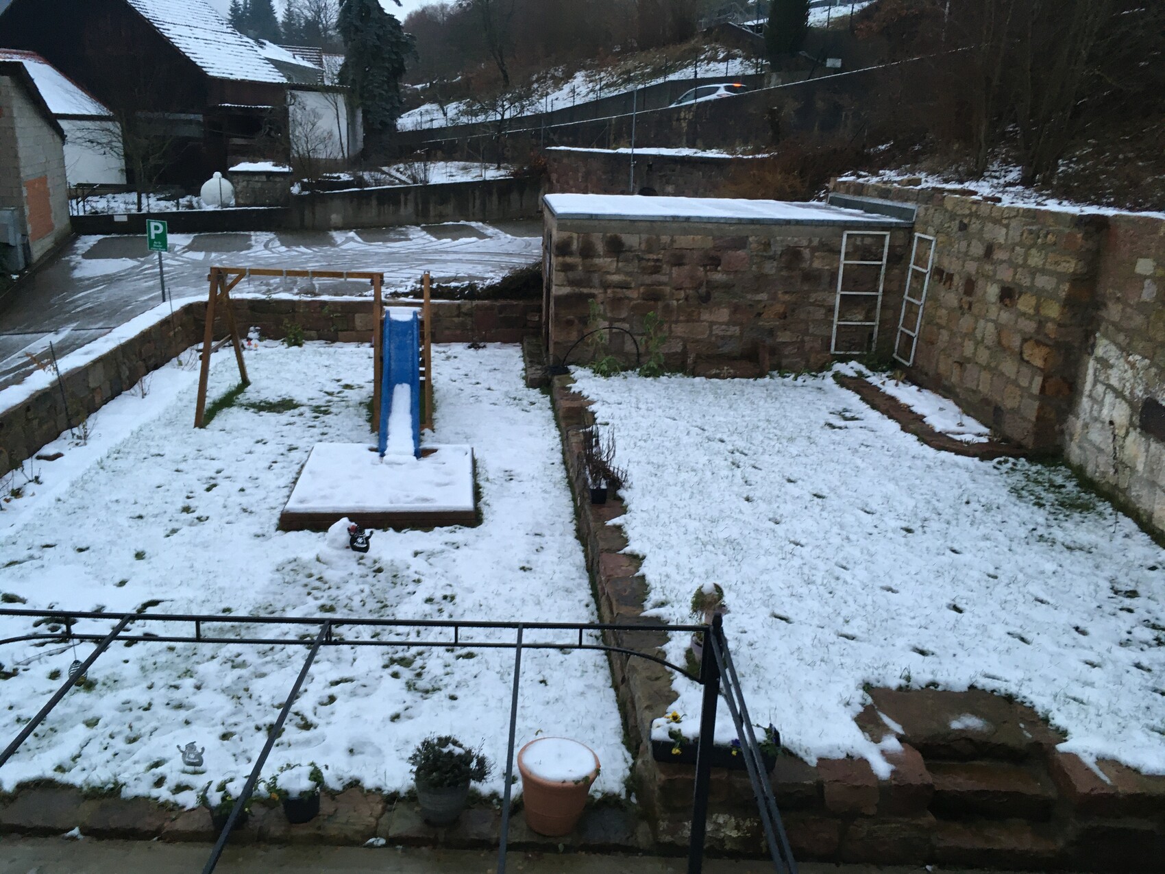 Snow-covered garden with blue play tower slide, stone walls and terrace.