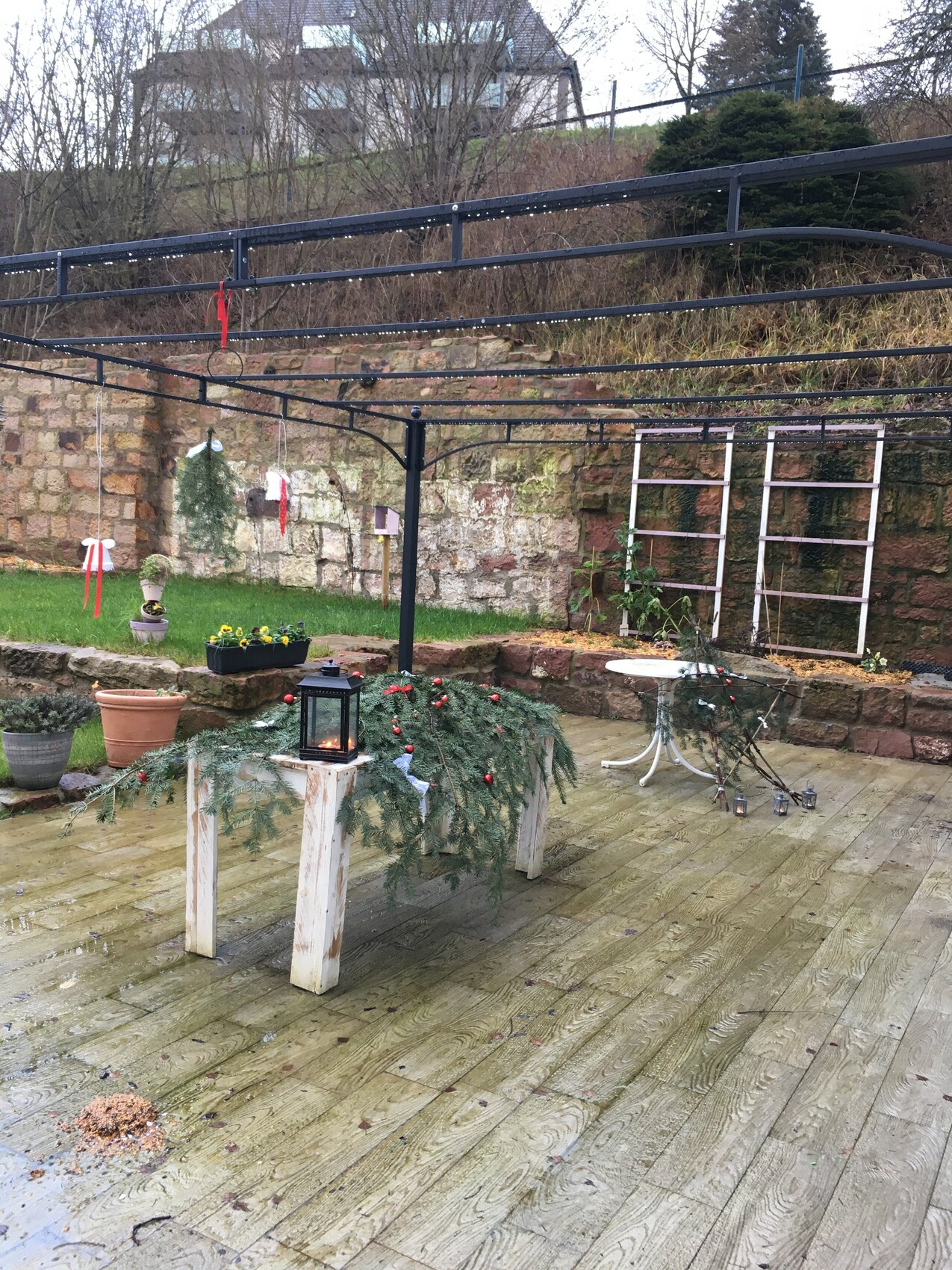 Garden terrace with wooden deck, lanterns, decorations and metal frames in front of stone wall