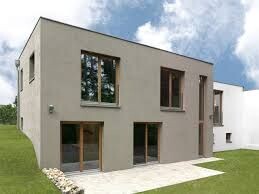 Moderne beige zweistöckige Hausfassade mit großen Fenstern, Terrassenbereich und grünem Rasen.