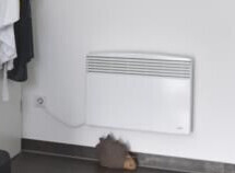 White panel radiator on a white living room wall, clothes hanging on the left.