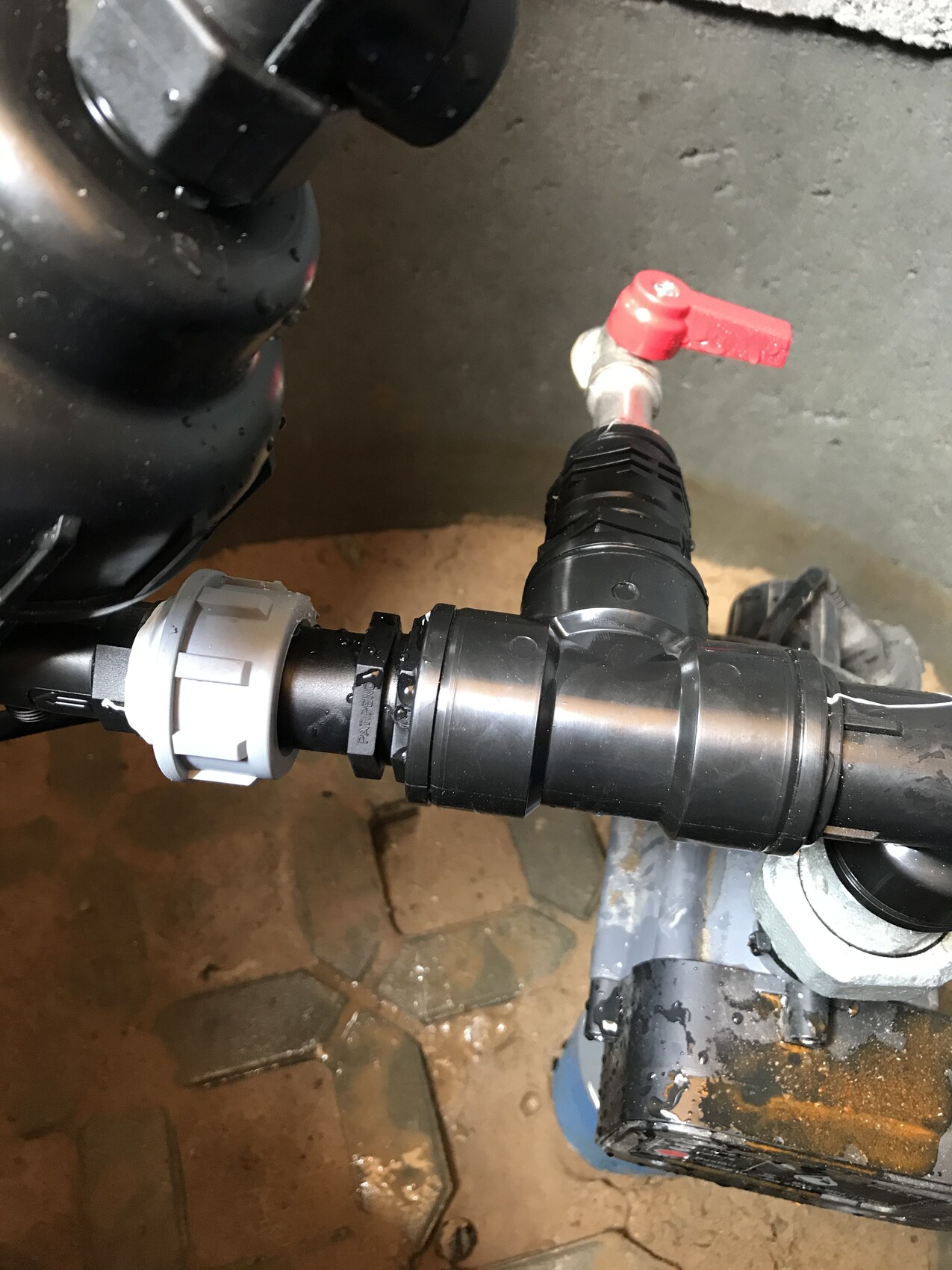 Black pipe with red shut-off valve, gray adapter, and connector on the floor.