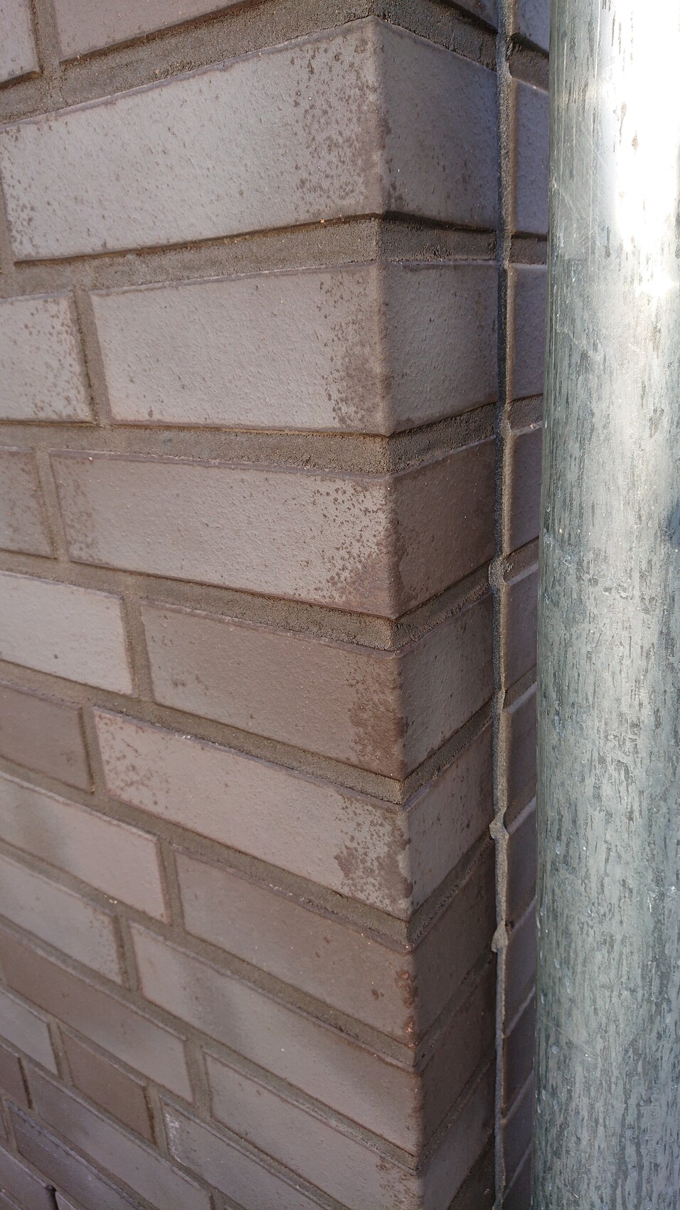 Corner view of a brown brick wall with a vertical metal pipe.