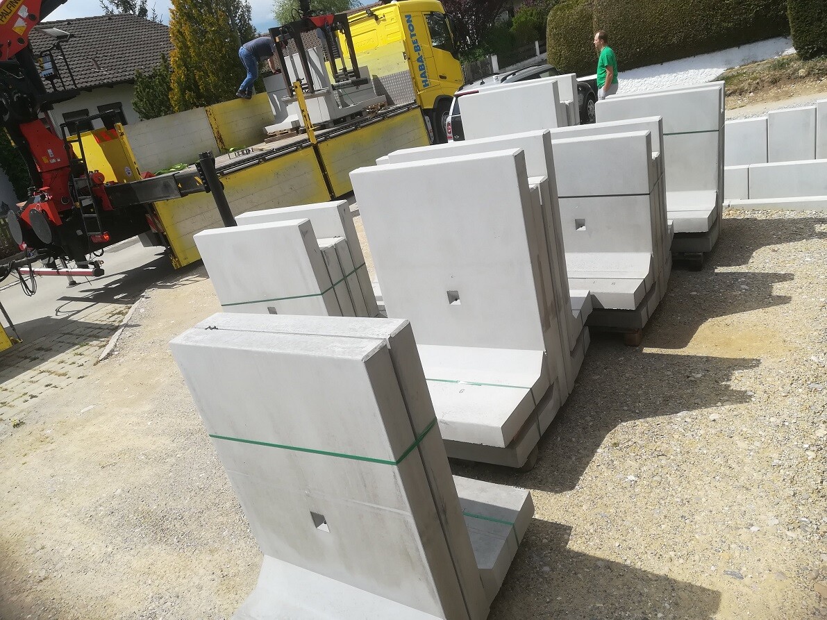 Large concrete slabs and supports on pallets, construction equipment visible, man in green shirt in the background.