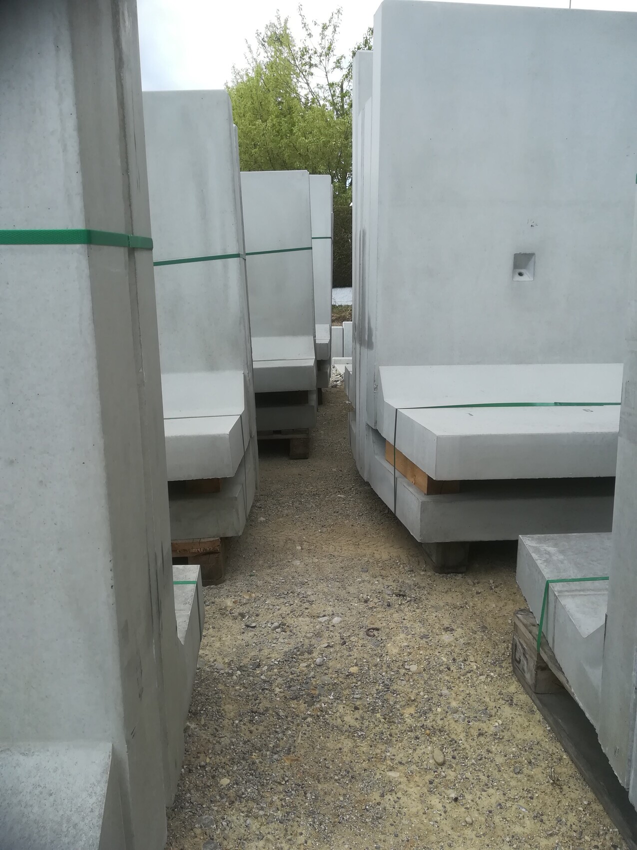 Large gray concrete slabs stacked on pallets, green straps, passageway between them.