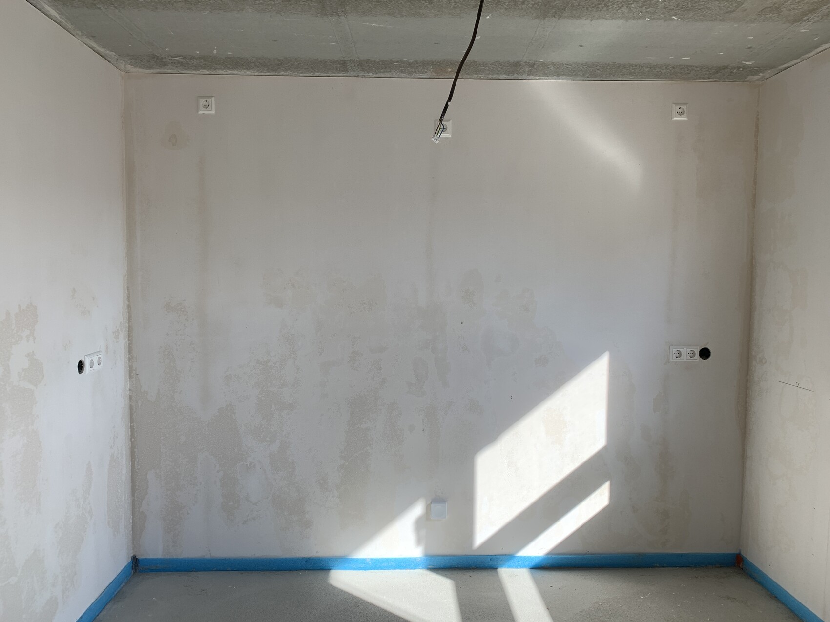 Unfinished room with plaster stains, open cable from the ceiling, blue floor trim, light.