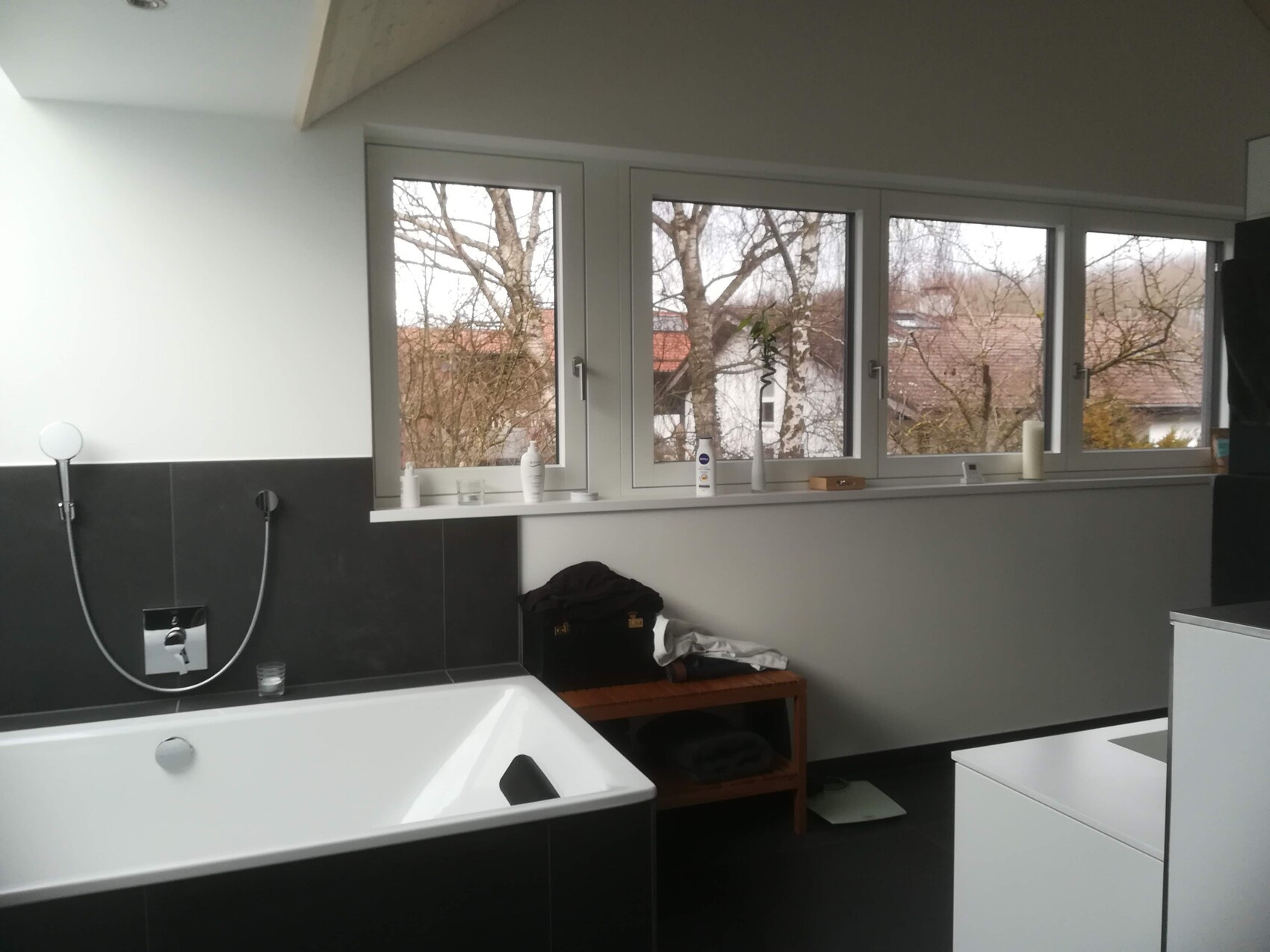 Modern bathroom with white bathtub, shower, window front and shelves.