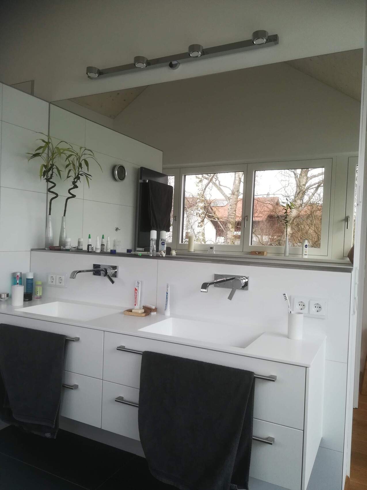 Modern bathroom with double washbasin, white cabinets, gray towels and window view.