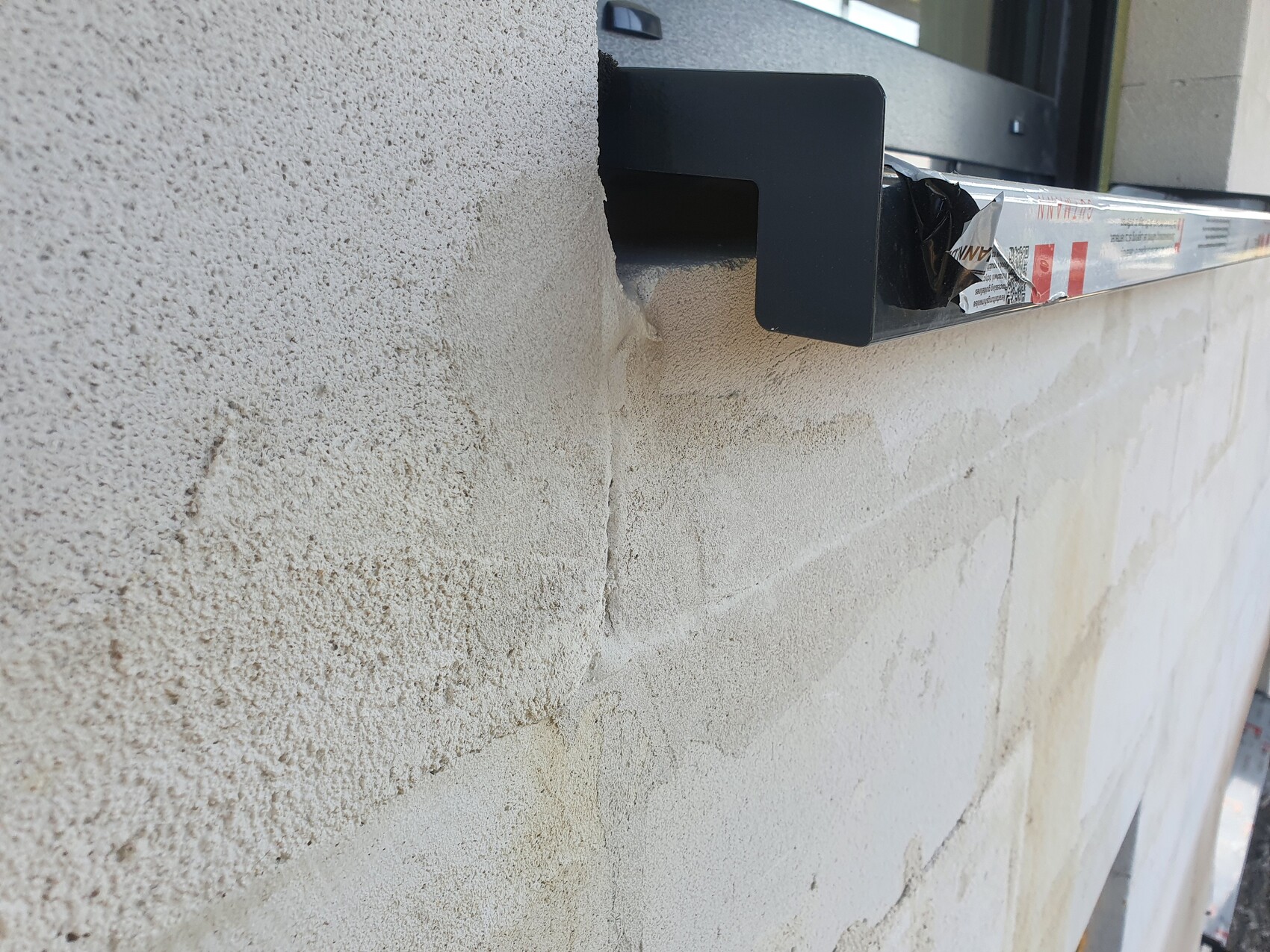Beige plaster wall with cracks and flaking; black window frame with tape.