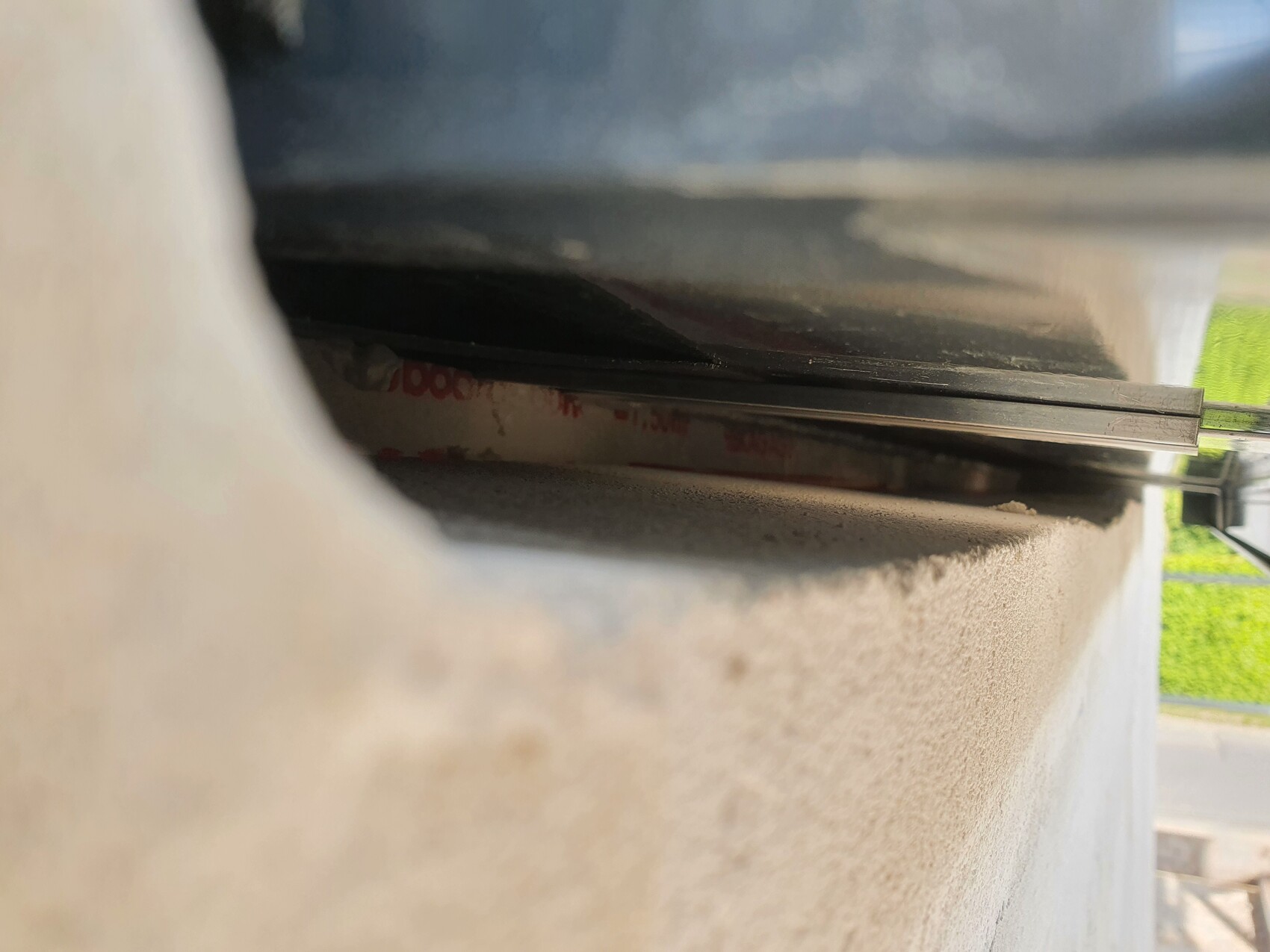 Close-up of a narrow gap between the wall and roller shutter guide; metal edge visible.