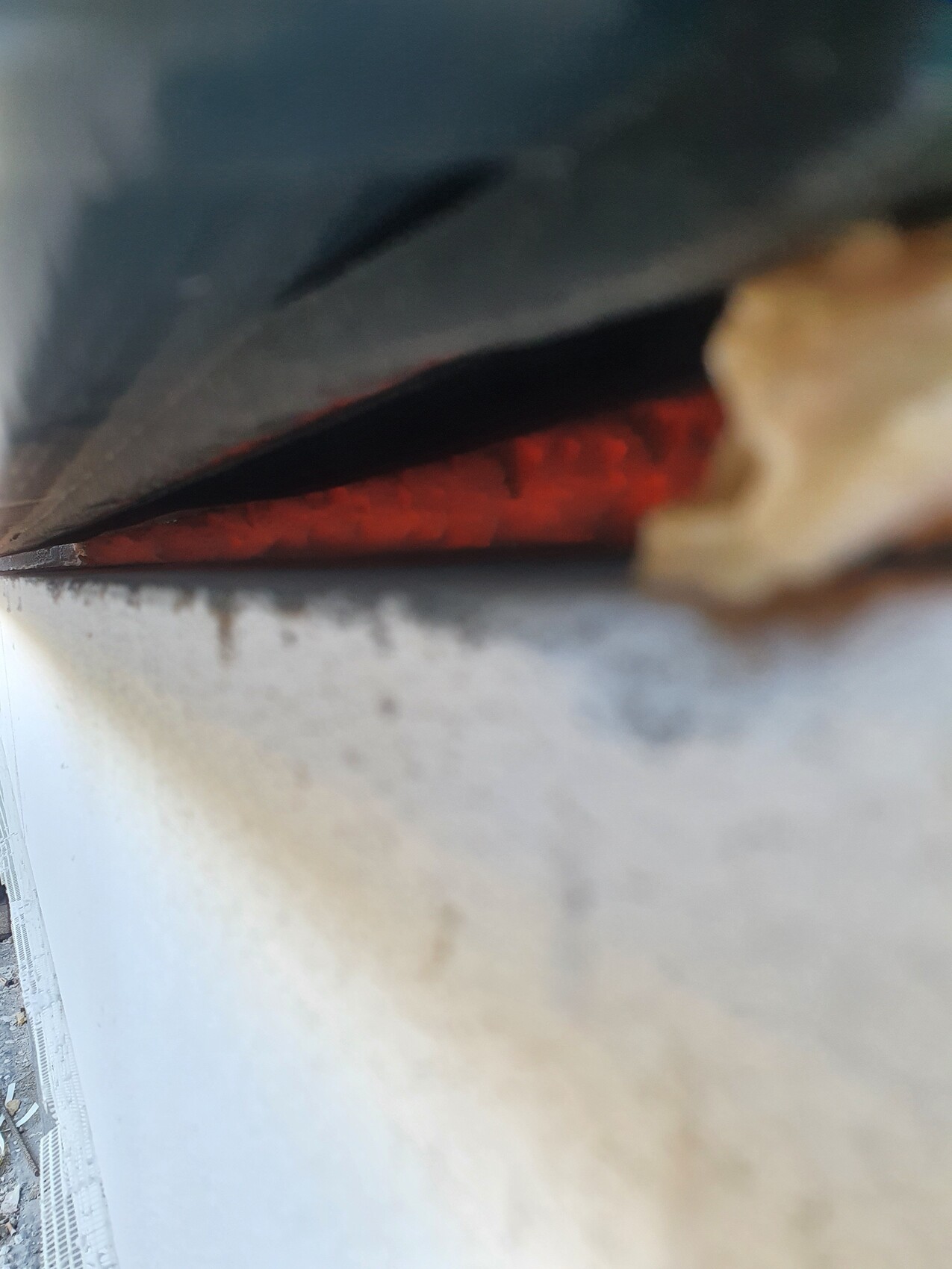 Close-up of a gap between a dark metal plate and a red interior surface.
