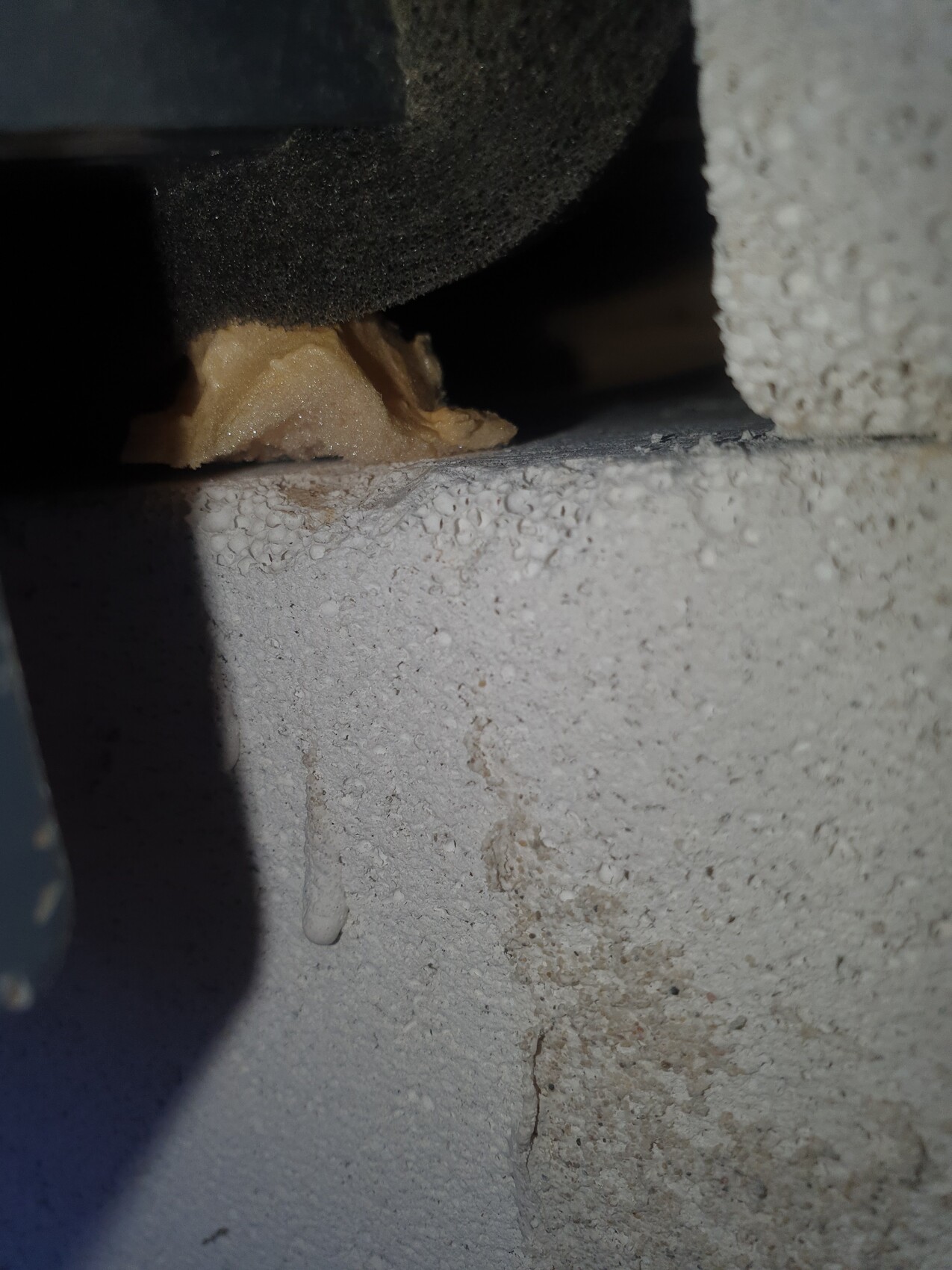 Detail of a gap in a concrete wall; beige adhesive residue, dark background, drops along the edge.