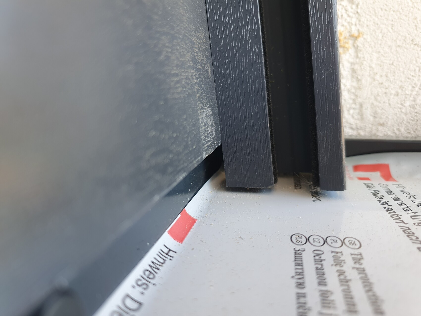 Two vertical dark wooden strips positioned between a black surface and a light-colored wall.