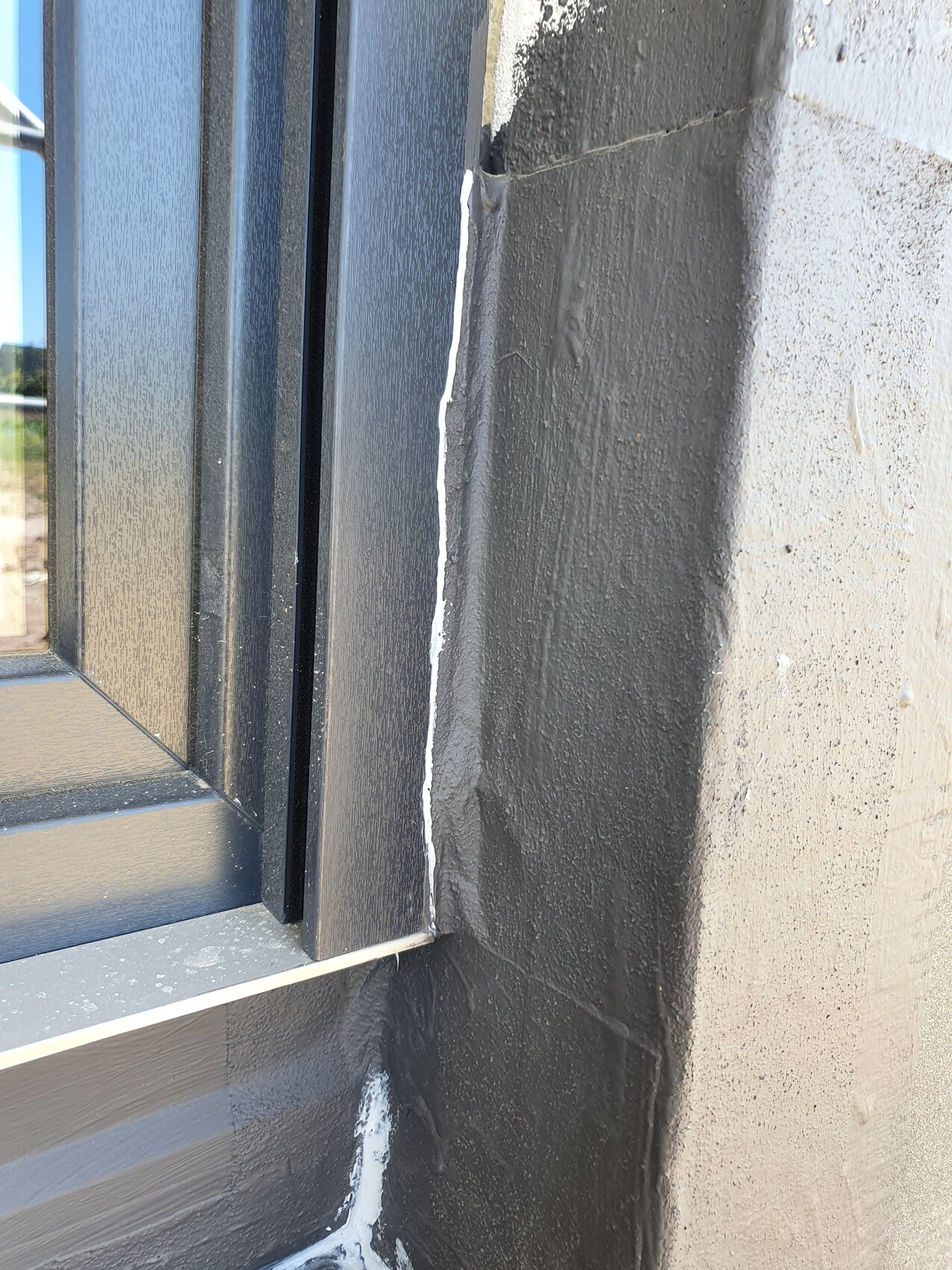 Window frame on gray wall; white sealant joint with visible crack.