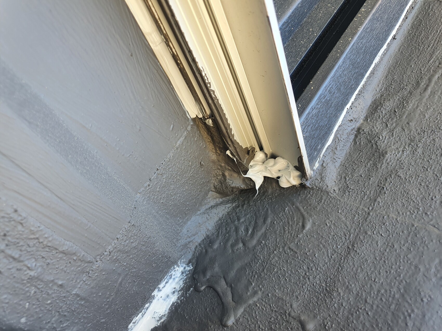 Exterior window frame with white sealant in the corner on gray masonry.