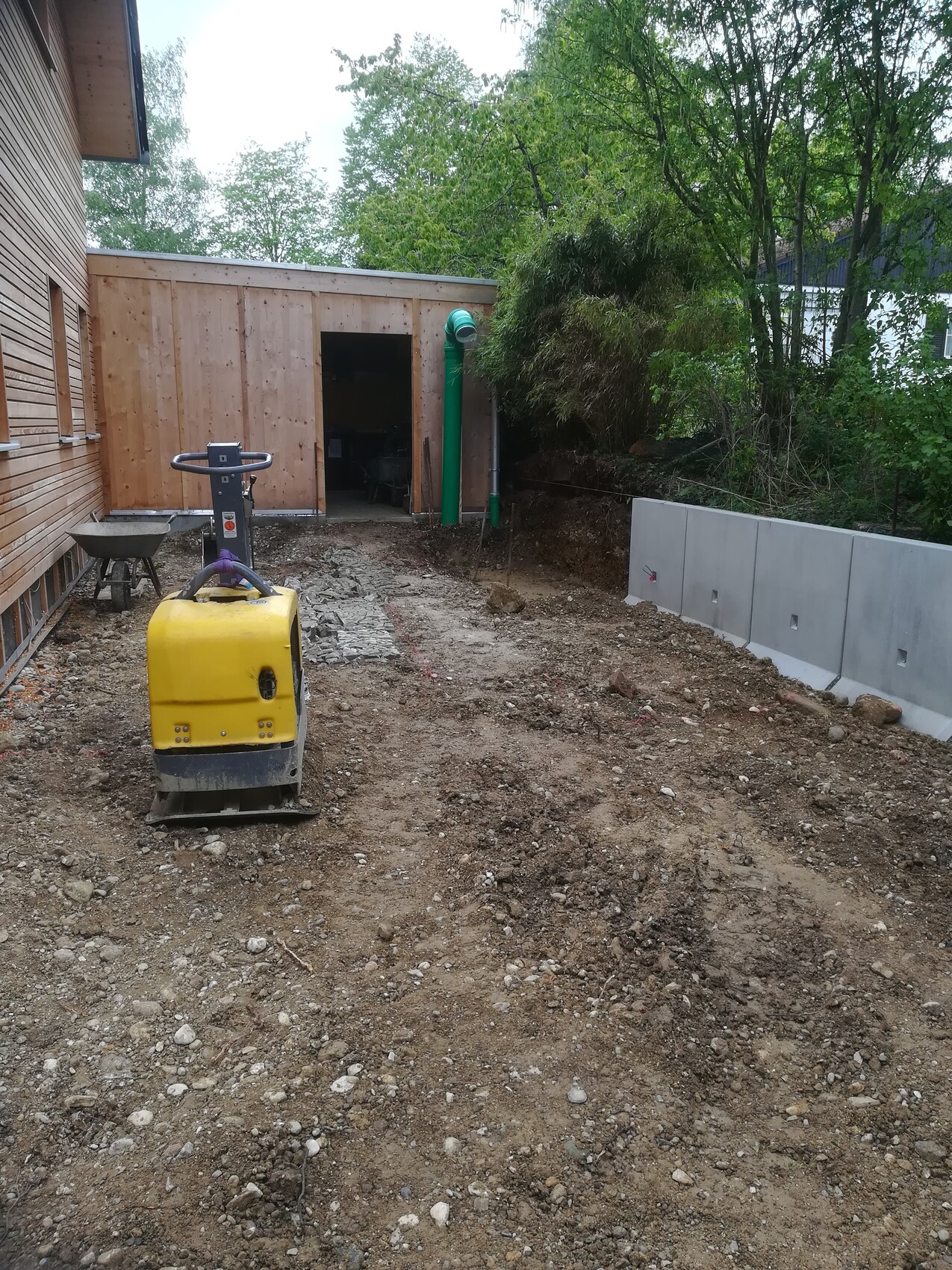 Backyard construction site: yellow plate compactor on unpaved ground next to wooden shed.