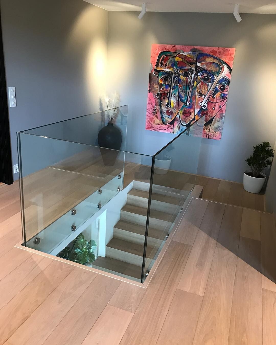 Modern staircase with glass railing; colorful abstract face painting on the wall, plant.
