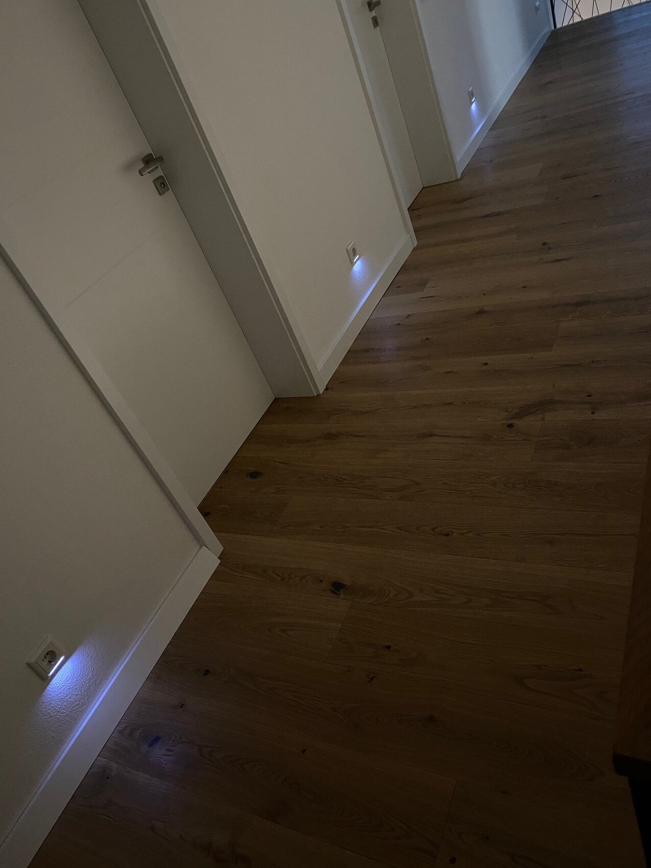 Bright hallway with wooden floor, white doors, and blue glowing LEDs on the floor.