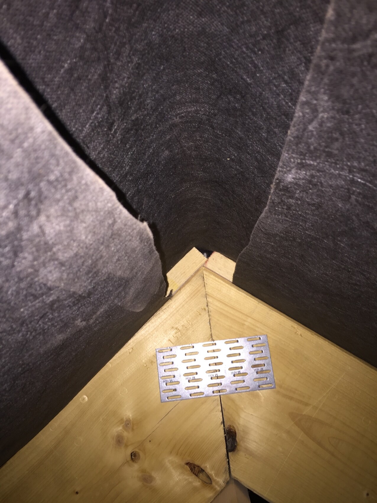 View into a corner of a wooden floor with metal mesh, dark wall sheathing, round opening in the back.