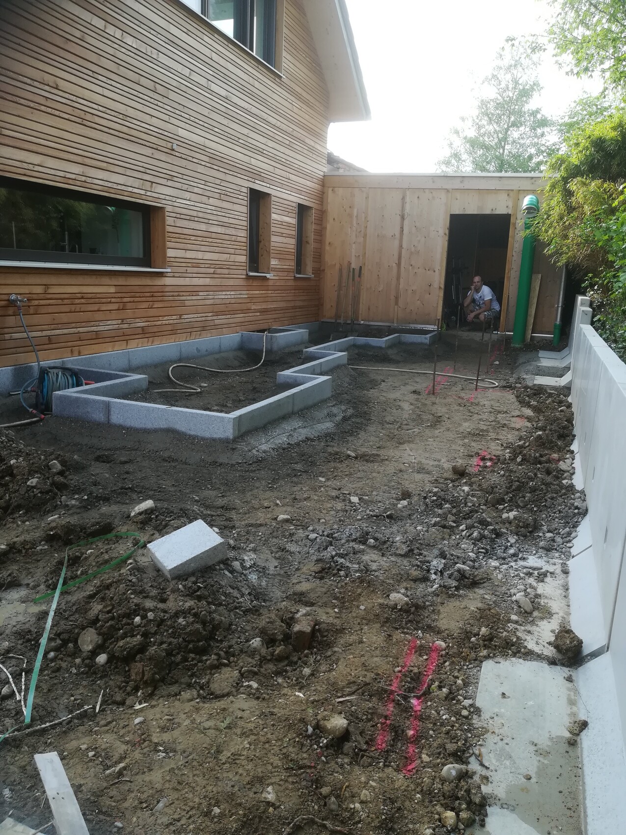 Garden construction site at the wooden house; concrete foundations made of blocks, worker in the shed.