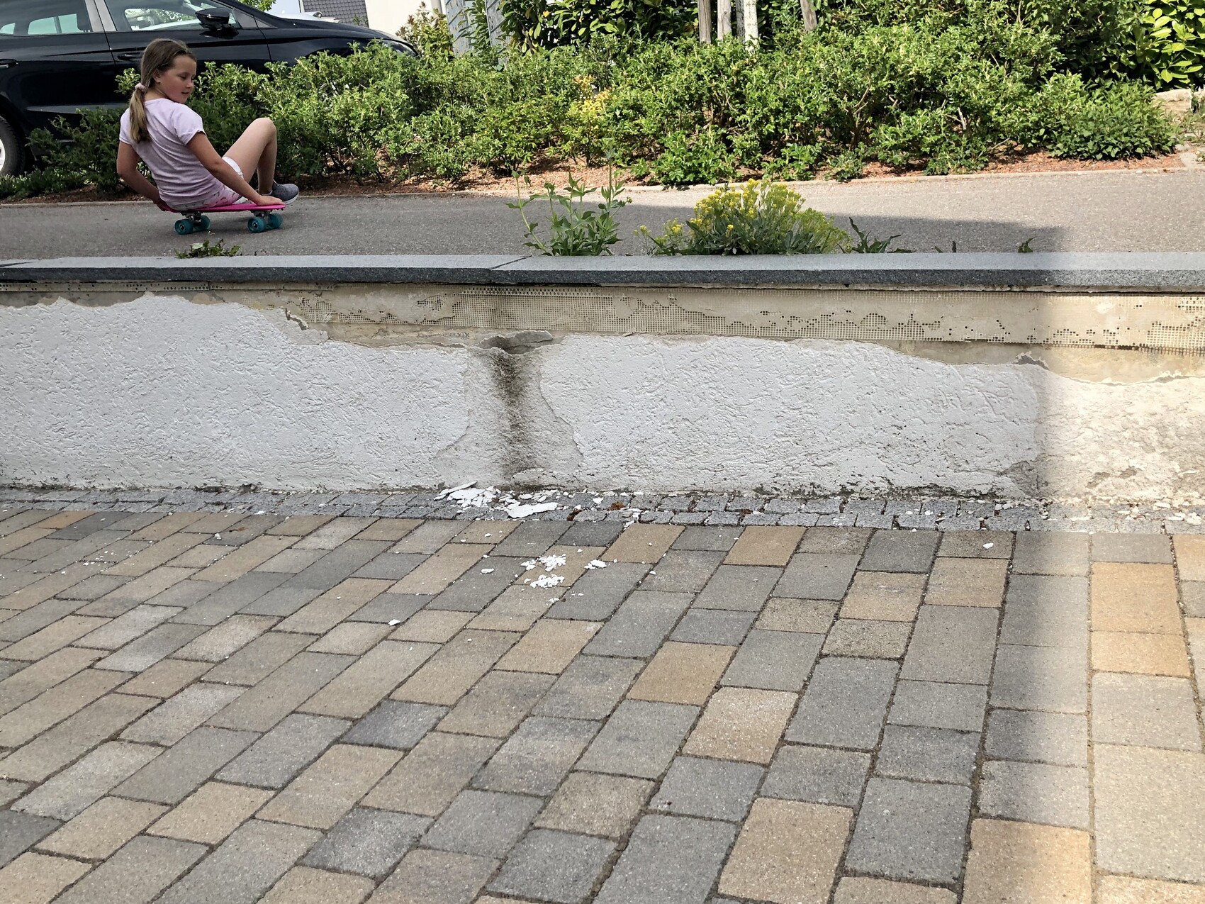Girl skating along a paved path next to a wall with garden plants.
