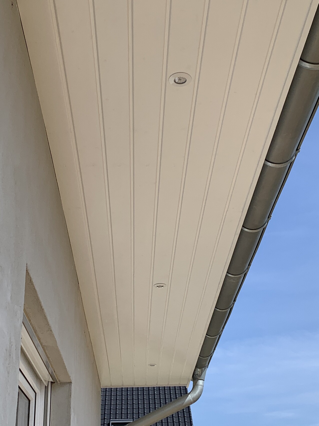 White cladding of the gutter with downpipe on the house wall, looking upwards.