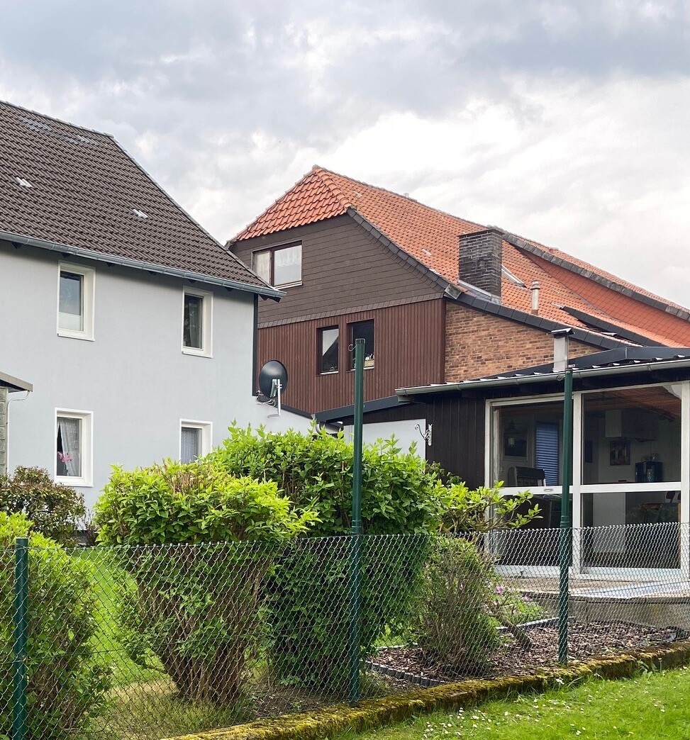 Siedlung mit grauen und braunen Häusern, Garten hinter Drahtzaun und verglaster Veranda.