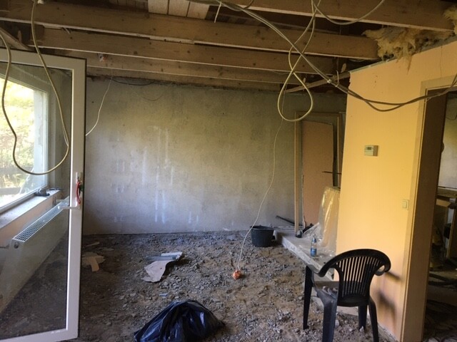 Unrenovated interior of a construction site: exposed ceiling beams, loose cables, debris, plastic chair.