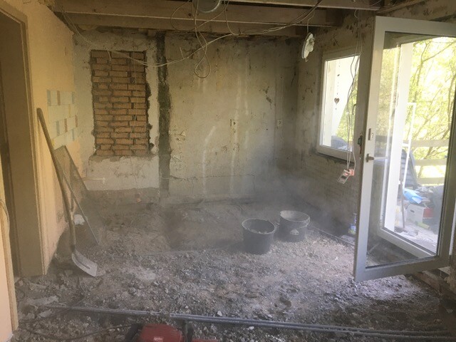 Shell living room: dust, unfinished floor, two buckets, open glass door leading outside.