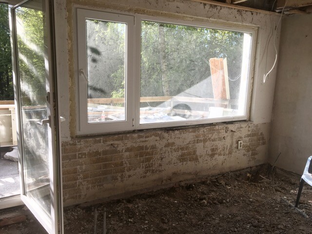 Renovation room with large window, exposed brick wall and debris on the floor.