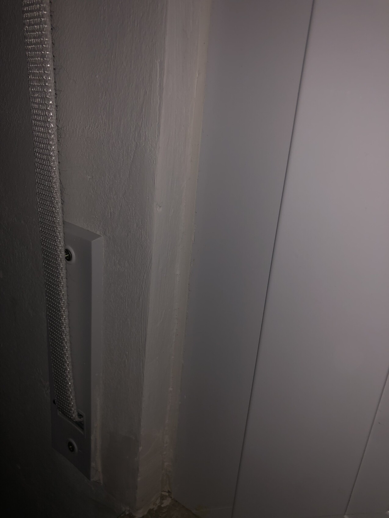 Close-up of a gray wall edge: on the left a vertical metal strip next to a smooth door cladding on the right.