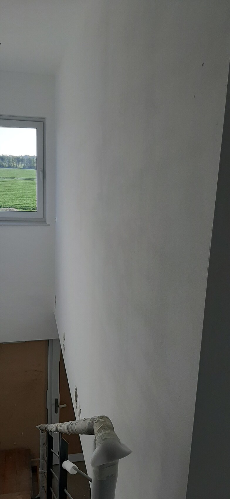 Heller Treppenaufgang in weißem Innenraum, Fenster mit Blick auf grüne Felder.