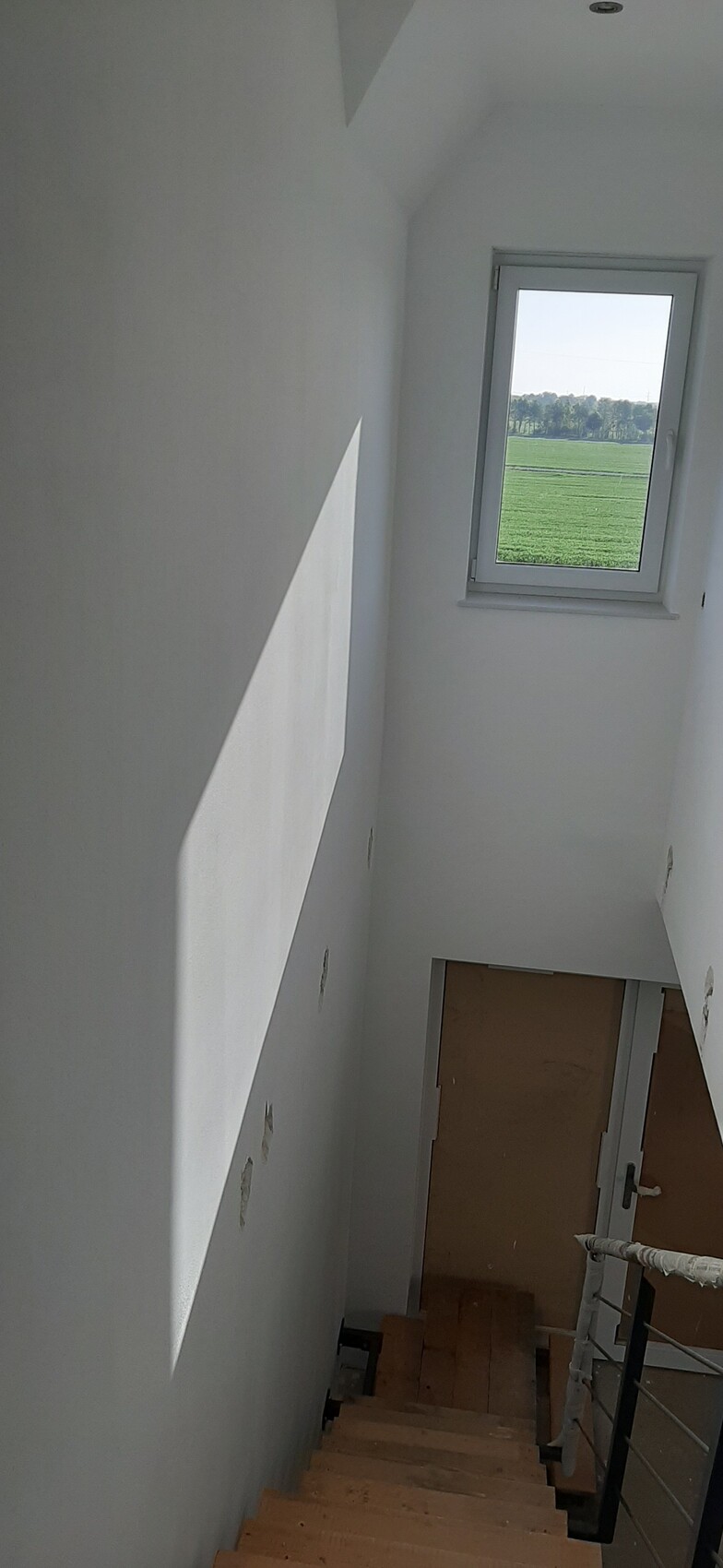 Heller Treppenaufgang im Innenraum eines Neubaus, weiße Wände, Fenster mit Blick auf ein grünes Feld.
