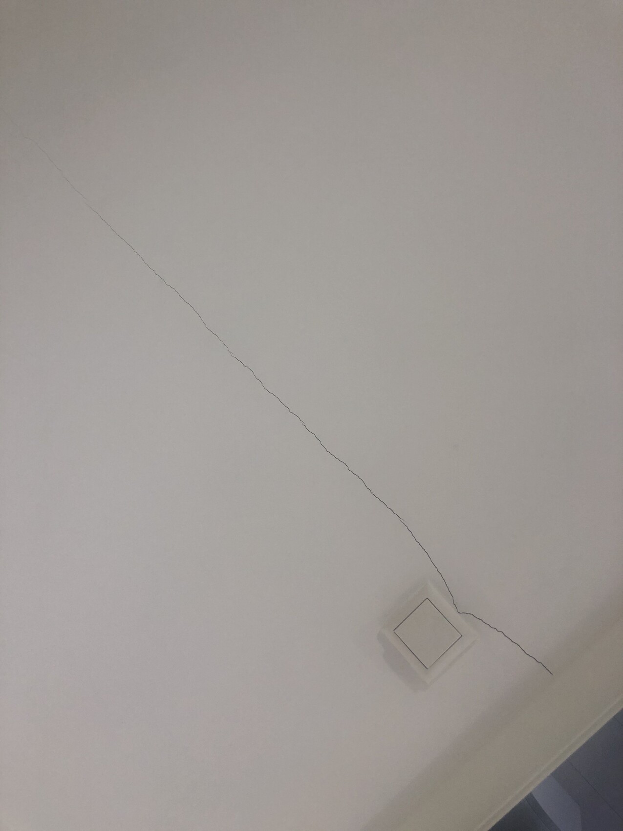 White ceiling with diagonal crack line, near a square ceiling light.