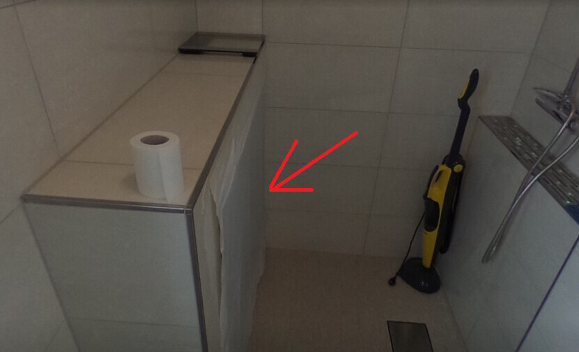 Small bathroom with gray tiles, yellow vacuum cleaner, toilet paper roll, white cloth.