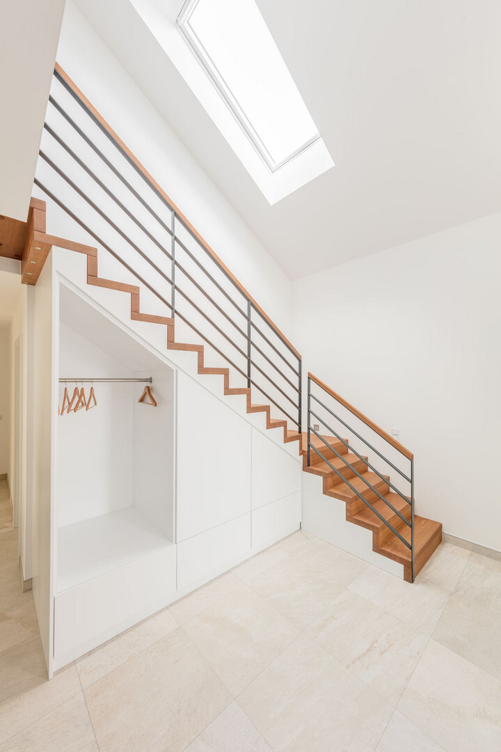 Bright entrance area with wooden stairs, metal railing, and open wardrobe under the stairs.