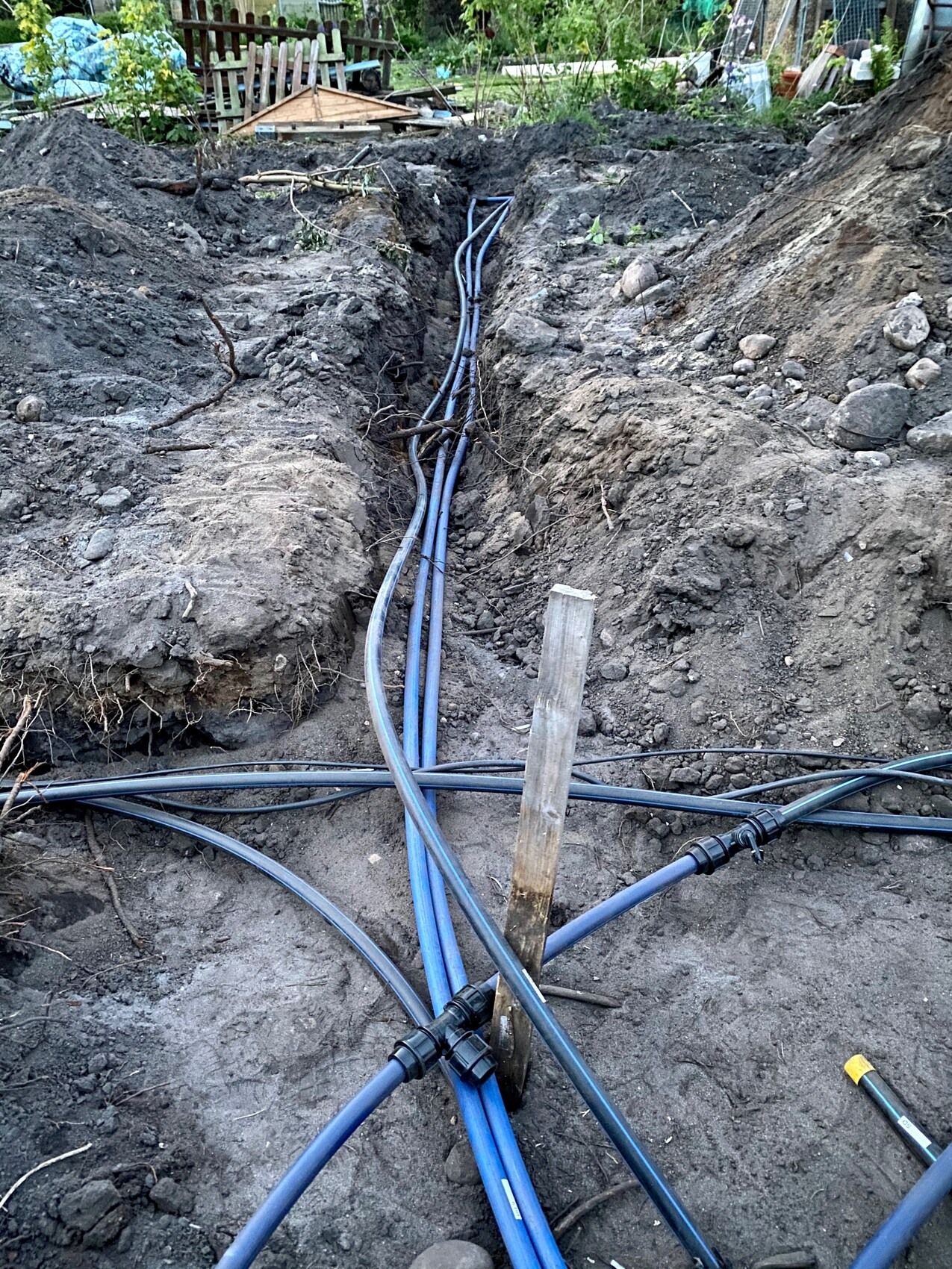 Graben mit blauen Kabelrohren und schwarzen Leitungen im Erdreich, Bauarbeiten im Garten.