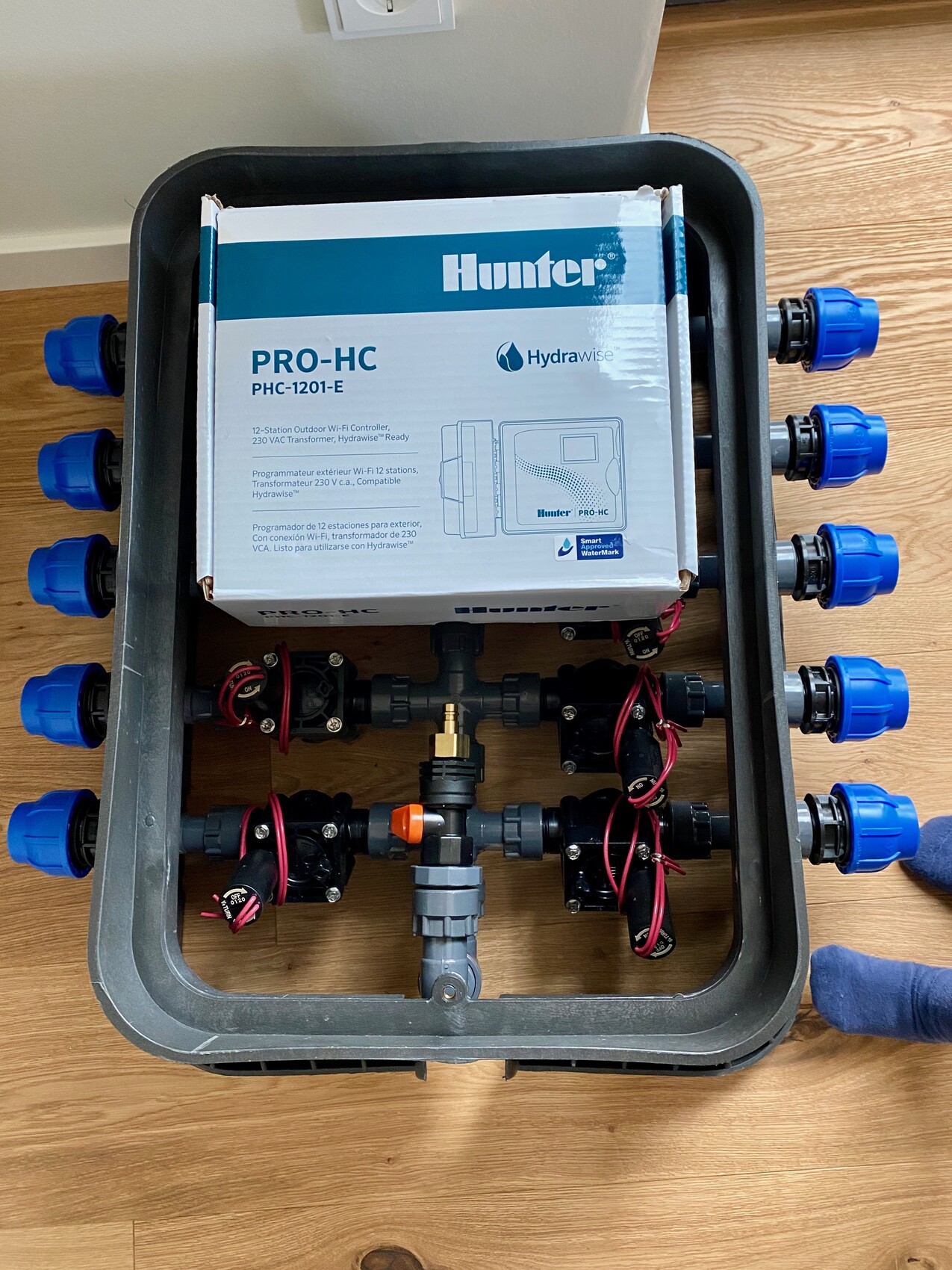 Hunter PRO-HC Hydrawise-Steuerung im Installationskasten mit blauen Anschlüssen und Ventilen.