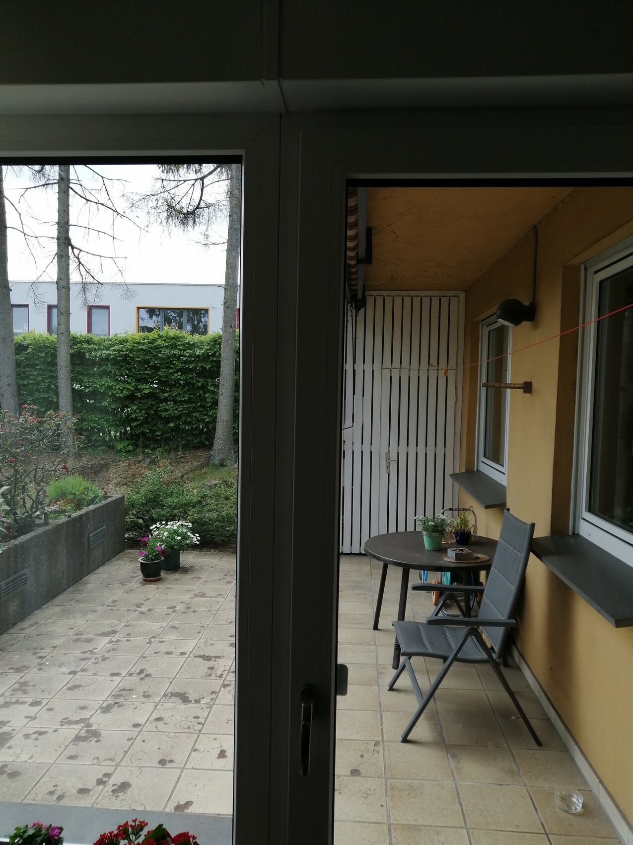 Balcony/veranda with round table, two folding chairs, potted plants; view of garden.