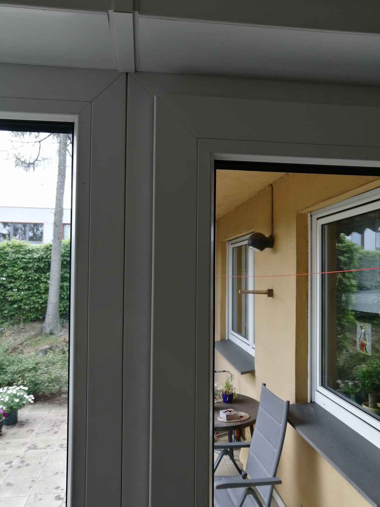 View through glass window onto balcony: yellow wall, table, chair, red clothesline, garden.