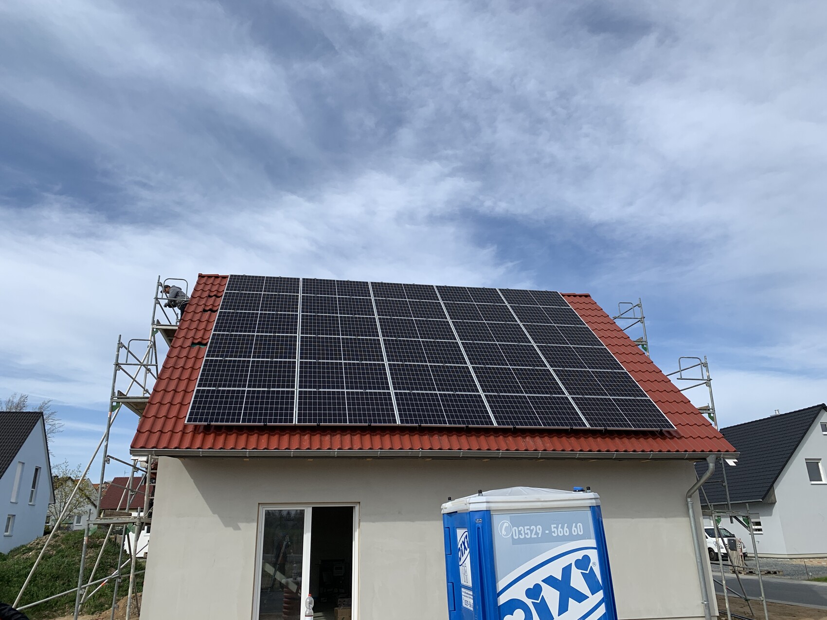 Roof of a house with solar panels, scaffolding, construction workers, blue sky.