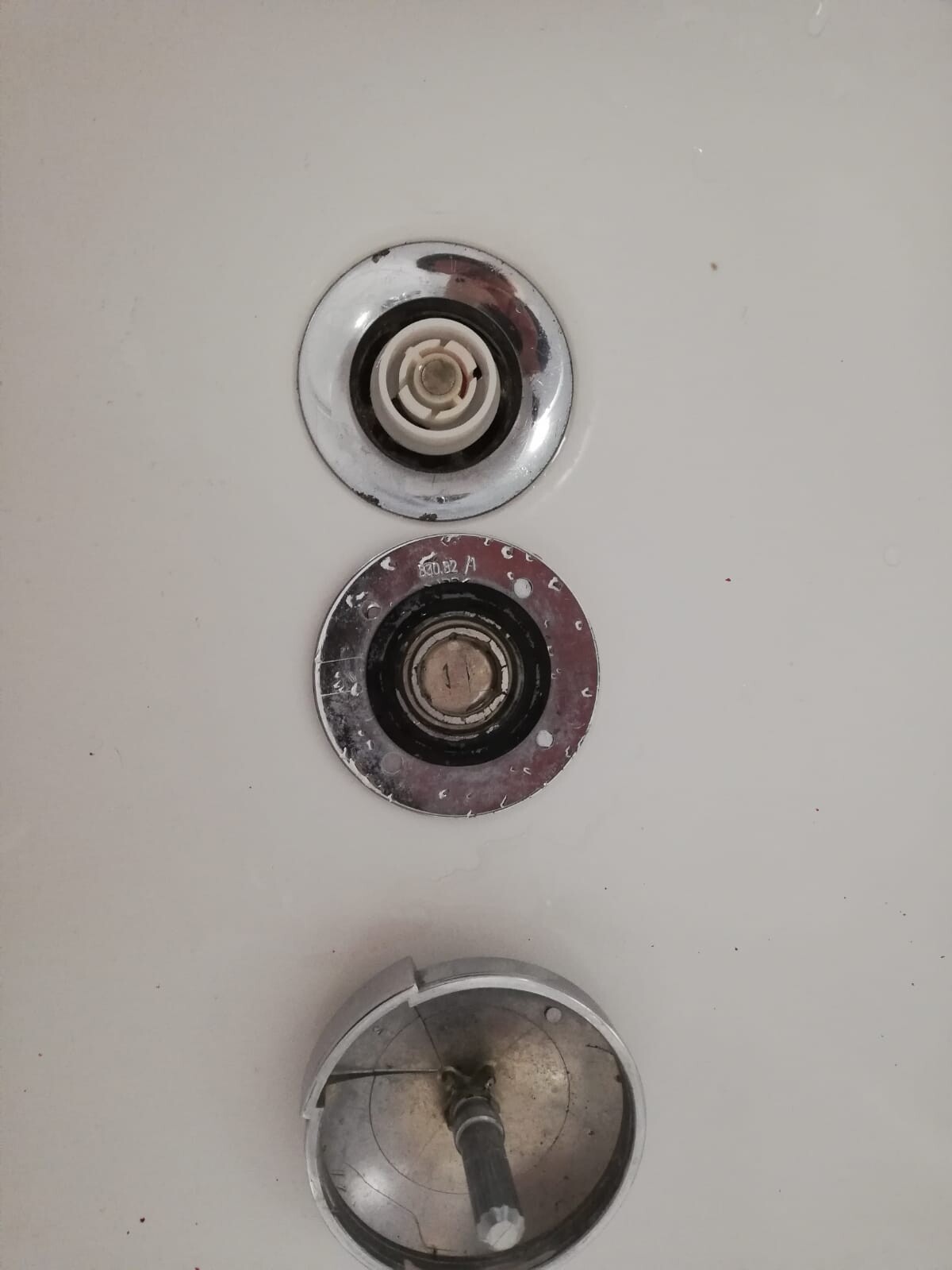 Three round plumbing valves arranged vertically on a white wall, visible with metal rings.