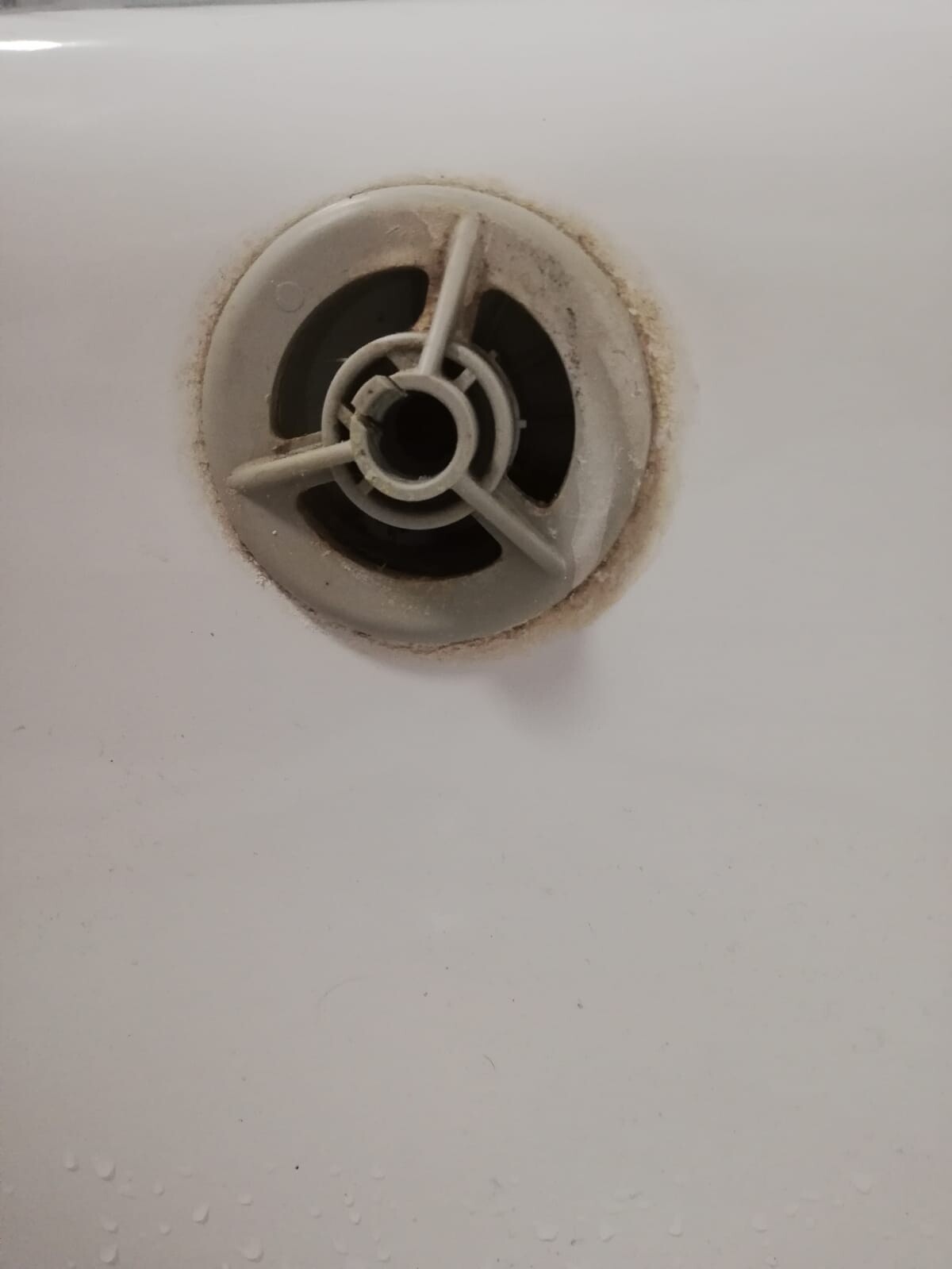 Round bathtub drain with plastic cover and dirt deposits around it.