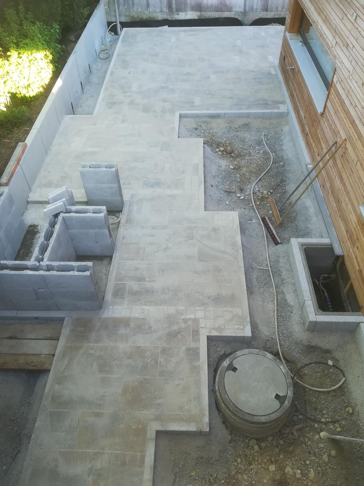 Drone shot of a garden construction site: light paving stones, concrete blocks, earthworks and wooden house.